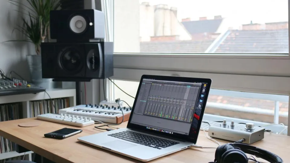 A laptop running audio editing software beside studio monitors and a keyboard