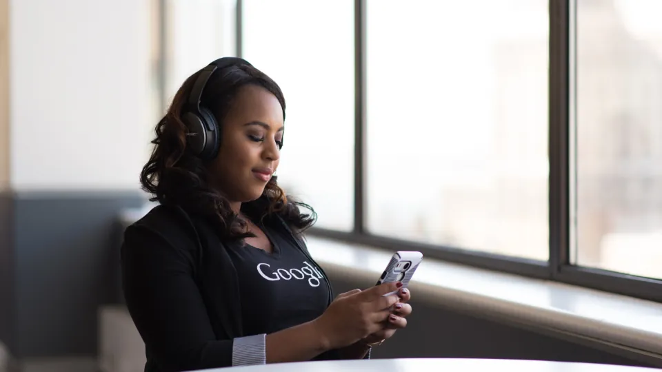 A woman listening on headphones while looking at her phone by a window