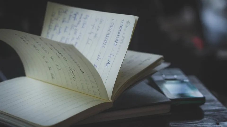 Open notebook with handwritten notes beside a pen on a dark desk