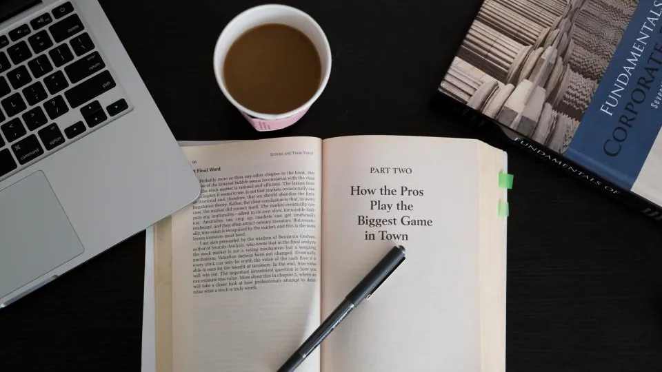 An open book, a cup of coffee and a laptop on a dark desk