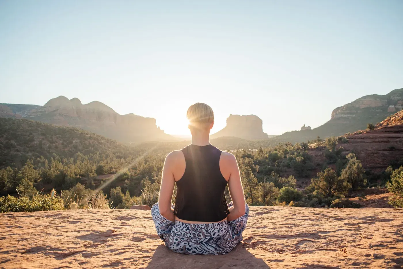 Person meditating in a cross-legged pose on a sunlit cliff at sunrise