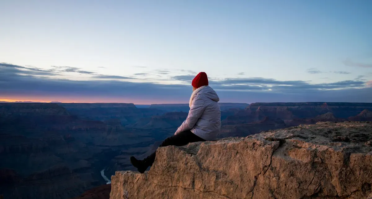 Person sitting on a canyon edge at sunset