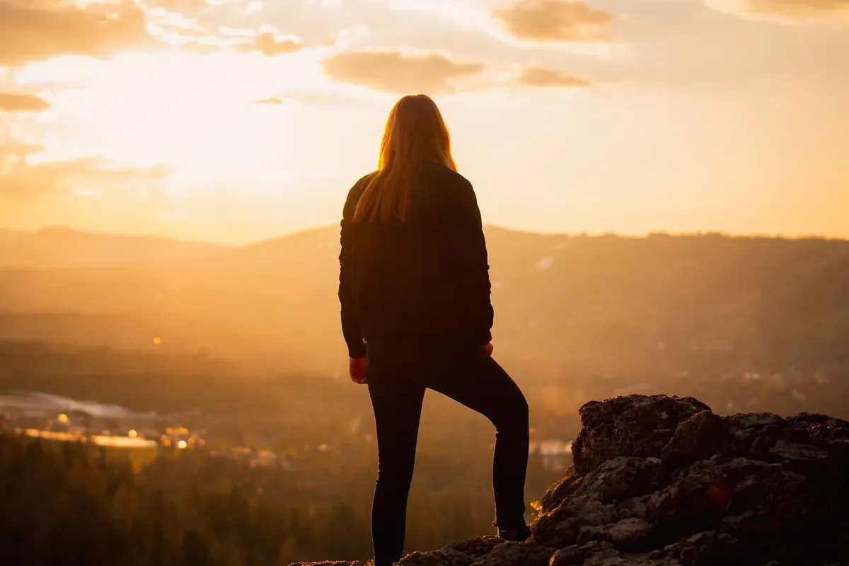 Woman watching the sunrise from a mountain rock