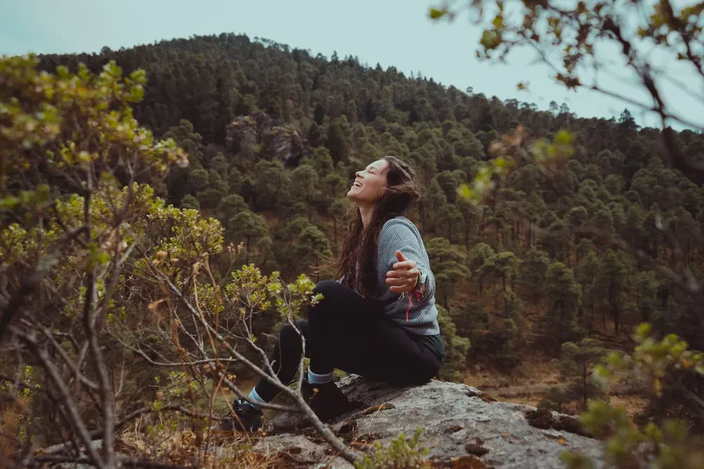 Happy woman sitting on a boulder in a forested mountain landscape