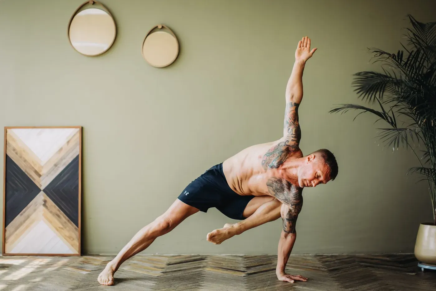 Man holding a balanced yoga pose in a calm, plant-filled room